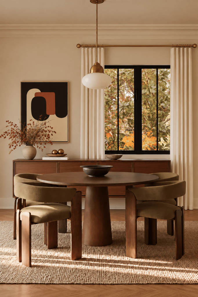 Japandi dining room with walnut table, olive upholstered chairs, abstract artwork, brass pendant, and early autumn foliage.
